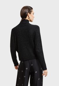 Crni, sjajni pleteni džemper s visokim ovratnikom i skraćenim dizajnom. Ima dugačke rukave i opušteni kroj, uparen s hlačama otpada.