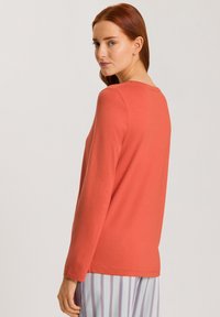 T-shirt de manga larga en tejido de jersey color coral con cuello redondo y dobladillo recto, combinado con pantalones de pijama a rayas.