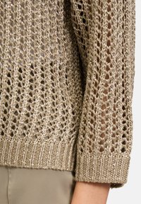 Pull en tricot beige avec un motif de mailles ouvertes, doté d'un ourlet côtelé et d'une finition texturée. Le tissu inclut des fils métalliques subtils.
