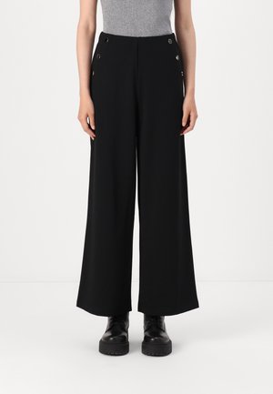 Pantalons larges noirs en tissu doux, avec une taille haute et quatre boutons dorés décoratifs à l'avant. Associés à des bottines noires.