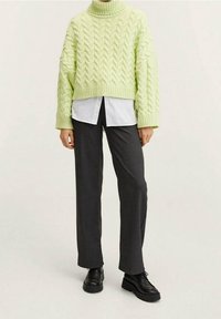 Un pull à col roulé en tricot torsadé vert clair associé à une chemise blanche à col et un pantalon droit gris foncé. Des chaussures noires à lacets complètent le look.