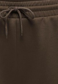 Dark brown sweatpants waistband with a tied braided drawstring and elastic ribbed detailing.
