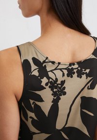 Top senza maniche con scollatura rotonda, caratterizzato da un motivo floreale nero su sfondo beige. Il tessuto appare morbido e leggero.