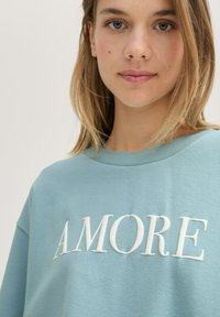 Light blue sweatshirt made of soft cotton, featuring the embossed word "AMORE" in white across the chest. Round neckline, relaxed fit.