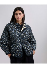 Chaqueta acolchada con un estampado de leopardo azul sobre un fondo negro, con un forro crema en contraste y botones negros, además de bolsillos laterales.