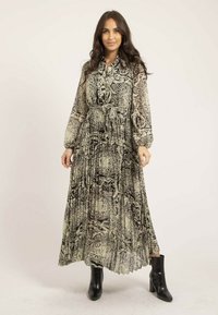 Robe longue en tissu transparent avec un motif complexe noir et blanc, un devant à boutons, une taille cintrée et des manches bouffantes, associée à des bottines noires.