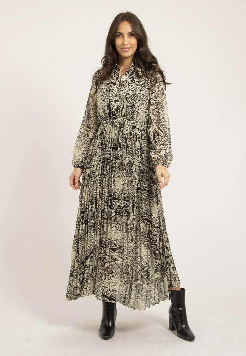 Robe longue en tissu transparent avec un motif complexe noir et blanc, un devant à boutons, une taille cintrée et des manches bouffantes, associée à des bottines noires.