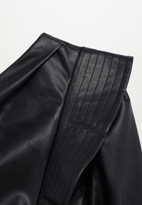 Chaqueta de cuero negra con hombro estructurado y costuras verticales, y una textura lisa en el cuerpo, que muestra un diseño elegante.