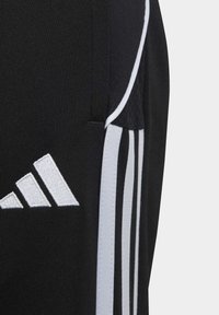 Schwarze Sporthose aus strukturiertem Stoff, mit drei weißen Streifen und einem weißen gestickten Logo am linken Bein.