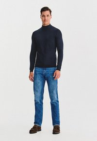 Granatowy golf wykonany z gładkiej tkaniny w połączeniu z jasnoniebieskimi dżinsami. Brązowe loafersy dopełniają strój, charakteryzujący się klasycznym krojem.