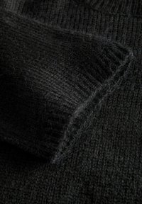 Tessuto nero a maglia con una finitura testurizzata e pelosa. Presenta bordi a coste, creando un aspetto caldo e morbido, adatto per l'uso in condizioni di freddo.
