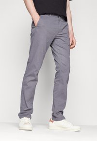 Šedé kalhoty se vzorem z lehkého materiálu, s úzkým střihem a předními kapsami. Kombinovány s bílými teniskami.
