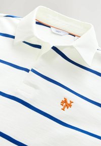 Valkoinen poolopaita, jossa on sinisiä vaakaraitoja, terävä kaulus ja vasemmassa rinnassa oranssi kirjailtu "N"-logo.