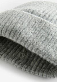 Chapeau en tricot gris avec une texture côtelée. Fabriqué en matériau doux semblable à de la laine, avec un revers replié et une finition légèrement duveteuse.