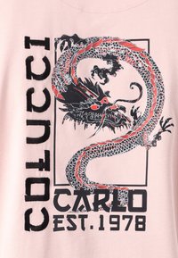 Light pink t-shirt featuring a large black and red dragon graphic, bold text "COLUCCI CARLO EST. 1978," and a textured fabric.