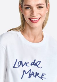 Weißes T-Shirt mit kurzen Ärmeln und Rundhalsausschnitt, das mit einem blauen Schriftzug "Lovedel Mare" bedruckt ist. Hergestellt aus glattem Baumwollstoff und im entspannten Schnitt.