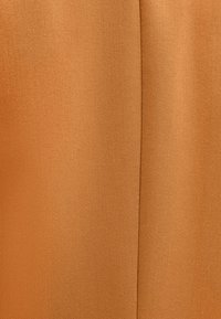 Gros plan sur un tissu de couleur rouille, présentant un tissage texturé avec un léger éclat. Surface lisse avec un pli vertical.