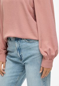 Ljust rosa texturerad långärmad topp med samlade manschetter, i kombination med högmidjade ljusblå denimjeans. Avslappnad passform med en ledig silhuett.