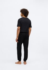 Crni kućni kompletić koji uključuje majicu s kratkim rukavima i sužene hlače. Mekana tekstura, opušteni kroj i elastični rukavi bez vidljivih uzoraka.