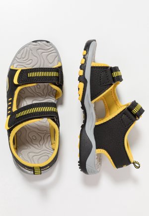 Czarno-żółte sportowe sandały dziecięce z regulowanymi paskami i teksturowaną szarą podeszwą, przedstawione z góry i z boku na białym tle.