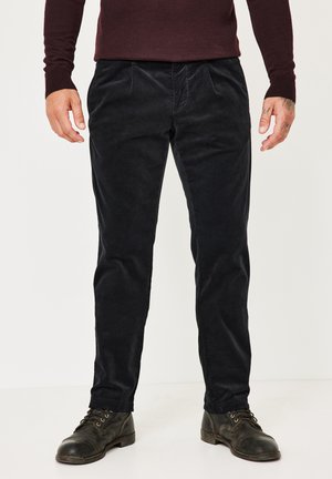 Dunkle Cordhose mit schmaler Passform, ausgestattet mit strukturiertem Stoff, vorderen Falten und Seitentaschen, kombiniert mit schwarzen Schnürstiefeln.