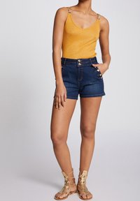 Gul, glittrig tanktopp med spagettiband och gyllene detaljer. Matchad med mörka denimshorts med hög midja och knappprysch.