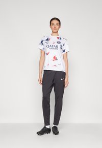 Hvit sports t-skjorte med blå og røde abstrakte design, med "Qatar Airways"-logo. Kombinert med svarte slim-fit bukser og svarte joggesko.