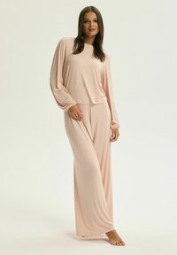Jasnoróżowy zestaw odzieży domowej z długim rękawem, z rękawami ze ściągaczami, oraz dopasowanymi szerokimi spodniami w miękkim materiale, zaprojektowany z myślą o komforcie.