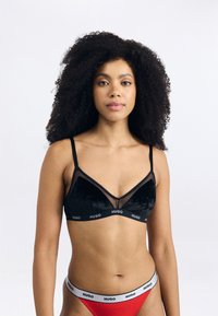 Bralette triunghiular din catifea neagră cu panouri transparente și margine ondulată, dotat cu un band elastic cu brand. Chiloți roșii cu un design similar al benzii.