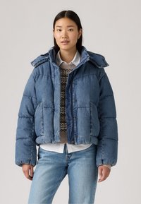 Denim puffer jacket in medium blue, met een capuchon, een ritssluiting en zijzakken. De textuur is zacht gewatteerd, met ribboorden.