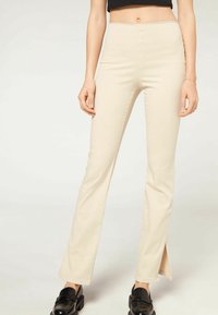 Pantaloni beige a vita alta a campana con gamba dritta e spacchi laterali, realizzati in un tessuto liscio. Abbinati a scarpe nere.