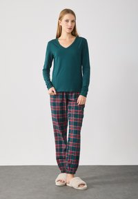 Teal langærmet top parret med grønternet bukser med røde og blå tern. Bukserne har elastisk talje og gummisålesko.