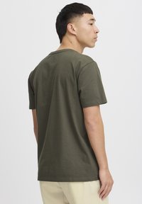 Tricou scurt cu mâneci în culoare verde măsliniu, din bumbac, având guler rotund și o croială lejeră, prezentat din spate, cu o textură netedă.