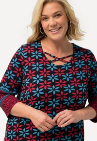 Zwart top met een multicolore bloemenpatroon, met rode en blauwe bloemen. Overlappend halsdetail en bloemenaccenten op de mouwen.