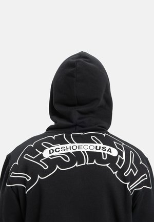 Zwarte hoodie met grote witte grafische tekst op de achterkant, met gebogen letters en de merknaam "DCSHOECUSA." Textuurstof, met capuchon.