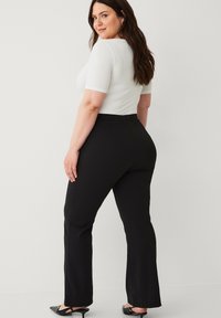 Sorte flared bukser med en glat tekstur, parret med en tætsiddende hvid top. Outfittet har en mellem-høj talje og et minimalistisk design.