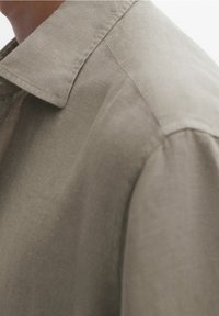 Lichtgrijze linnen shirt met een kraag, voorzien van een gestructureerde stof en een losse pasvorm, met gedetailleerde stiksel langs de naden.