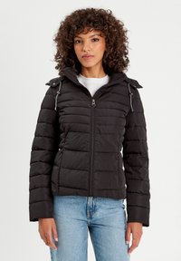 Veste matelassée noire avec fermeture éclair à l'avant, capuche réglable et poches latérales. Présente un design matelassé et une coupe courte. Texture lisse.