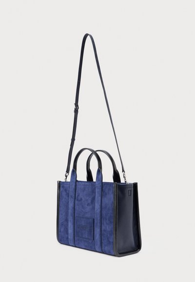 Bolso de ante azul marino con detalles en cuero negro, que cuenta con dos asas superiores y una correa de hombro ajustable. Forma estructurada con detalle de logotipo.