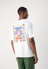 Camiseta de algodón blanca con un diseño gráfico colorido en la parte trasera que presenta el texto "TU MENTE LIBRE" y formas abstractas en varios colores pastel.