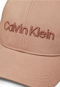 Pink baseball cap made of smooth fabric featuring embossed "Calvin Klein" logo in matching thread. Visor with stitched detailing.