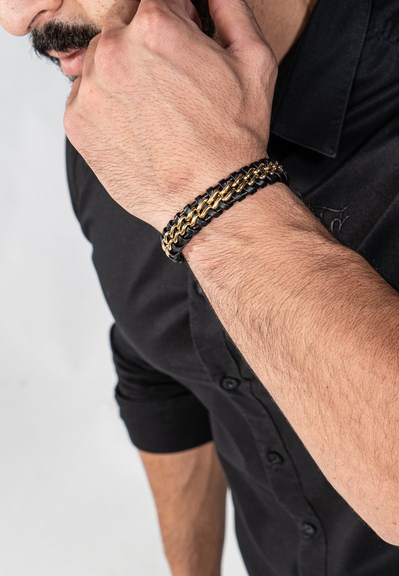 Geflochtener schwarzer Lederarmband mit goldenen Metallakzenten; die taktile Textur kontrastiert mit den glatten Gliedern und ist so gestaltet, dass sie bequem am Handgelenk sitzt.