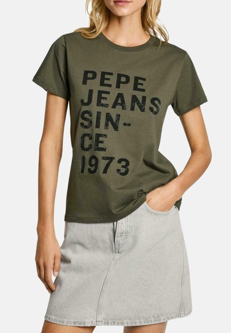 Camiseta verde olivo de manga corta, con texto negro "PEPE JEANS SINCE 1973" en un acabado texturizado y semibrillante. Combinada con una falda gris claro.
