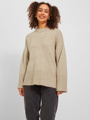 Beige kötött pulóver széles bordázott aljjal és ujjal. Puha textúra, laza szabás. Sötét szürke, laza farmernadrággal párosítva.