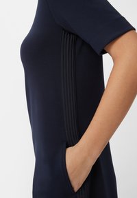 Navy Kleid mit schmaler Passform, kurzen Ärmeln, strukturiertem Seitendetail und einer Vorderasche. Glattes Gewebe mit subtiler sheen.
