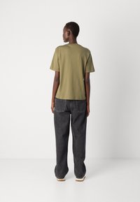 Olivenfarbene Baumwoll-T-Shirt mit kurzen Ärmeln, lockerer Passform und Rundhalsausschnitt, kombiniert mit schwarzen weit geschnittenen Jeans.