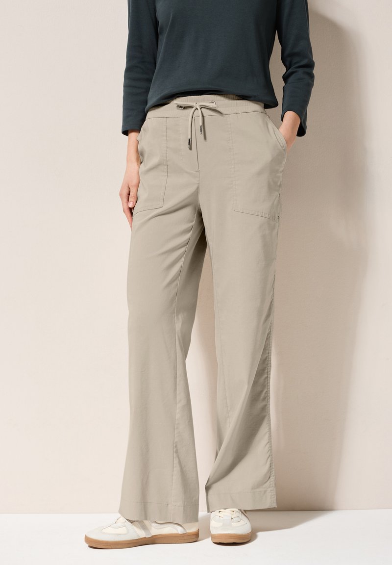Beige wijde broek met een aansnoerbare taille, zijzakken en een soepele, lichte stof. Gestyled met een donkere top en casual schoenen.