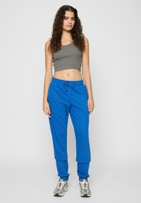 Modré bavlnené tepláky s elastickým pásom a šnúrkou, spárované so šedým crop topom. Modelka má na sebe šedé a biele tenisky.