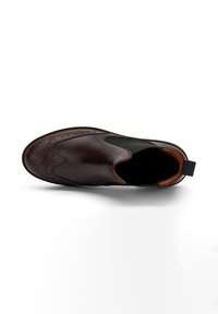 Zapato marrón de cuero tipo slip-on con detalles de brogue, paneles laterales elásticos y un interior naranja en contraste. Suela plana con una lengüeta en el talón.
