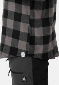 Camicia a quadri nera e grigia con un'etichetta che recita "DENIM FACTORY", indossata sopra dei pantaloni neri con tasca con zip e logo.